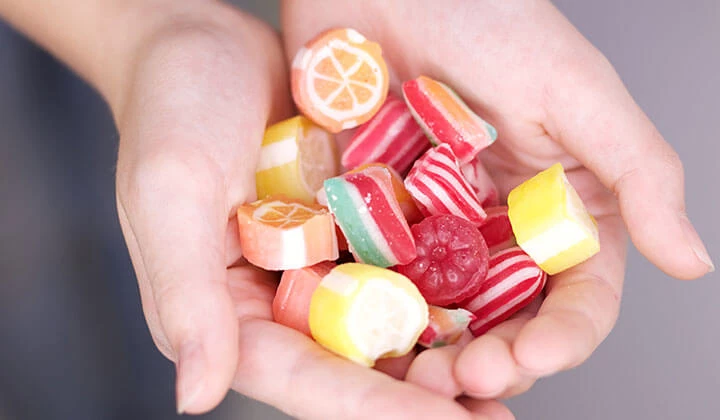 Hand mit Süßigkeiten Zahnfleischentzündung durch Zucker